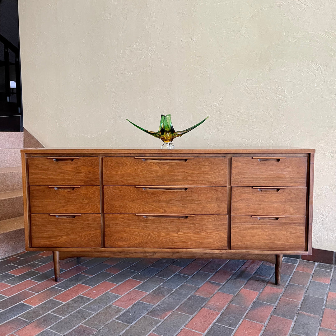 Enhance your bedroom with this Vintage KRUG Walnut 9 Drawer Dresser. The warm, rich color of the walnut complements any decor. Its sleek handle pulls add a touch of elegance to the design. With 9 spacious drawers, this dresser provides ample storage. 