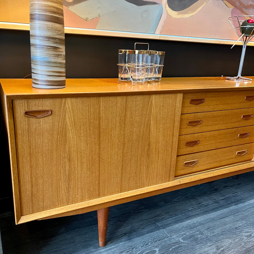 1960s Danish Teak Credenza is a beautiful blend of mid-century design and functionality. Crafted from teak, it features two sliding doors on either side that open to reveal ample storage space with adjustable shelving