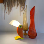 Colorful vintage toucan table lamp with glowing white shade, orange body and yellow base