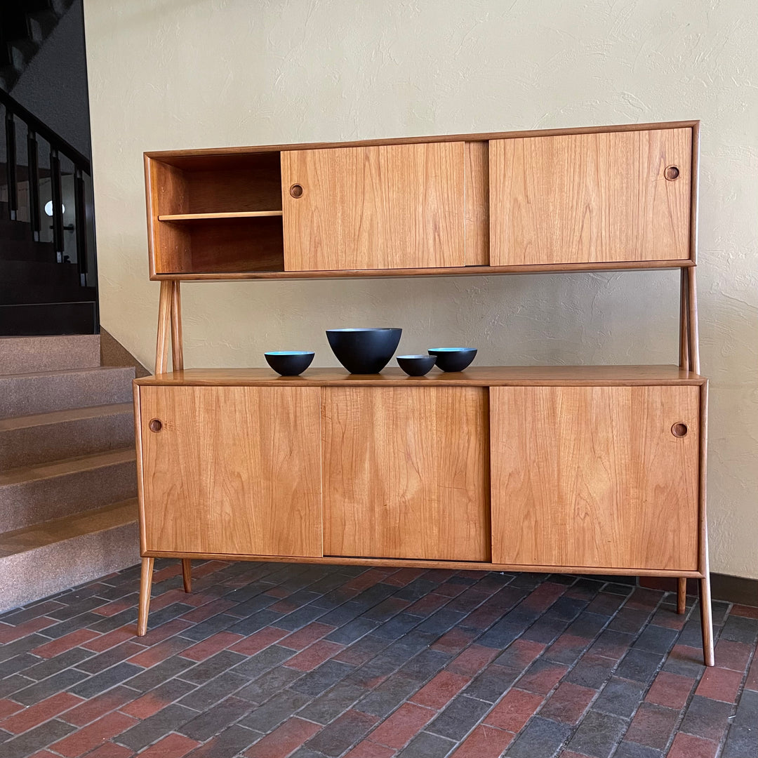 Two-tier Teak Danish Sideboard Credenza. The upper tier hosts a cabinet with sliding doors for storage. Below, sliding doors open to compartments with adjustable shelves, and drawers for small items. Solid sculptural teak legs tie the piece together. | Mr. Mansfield Vintage.
