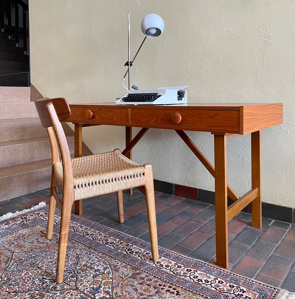  This Mid Century Danish Teak Desk epitomizes timeless design with its sleek lines and warm teak wood. Featuring two drawers, it offers practical storage while maintaining a minimalist aesthetic.