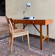  This Mid Century Danish Teak Desk epitomizes timeless design with its sleek lines and warm teak wood. Featuring two drawers, it offers practical storage while maintaining a minimalist aesthetic.