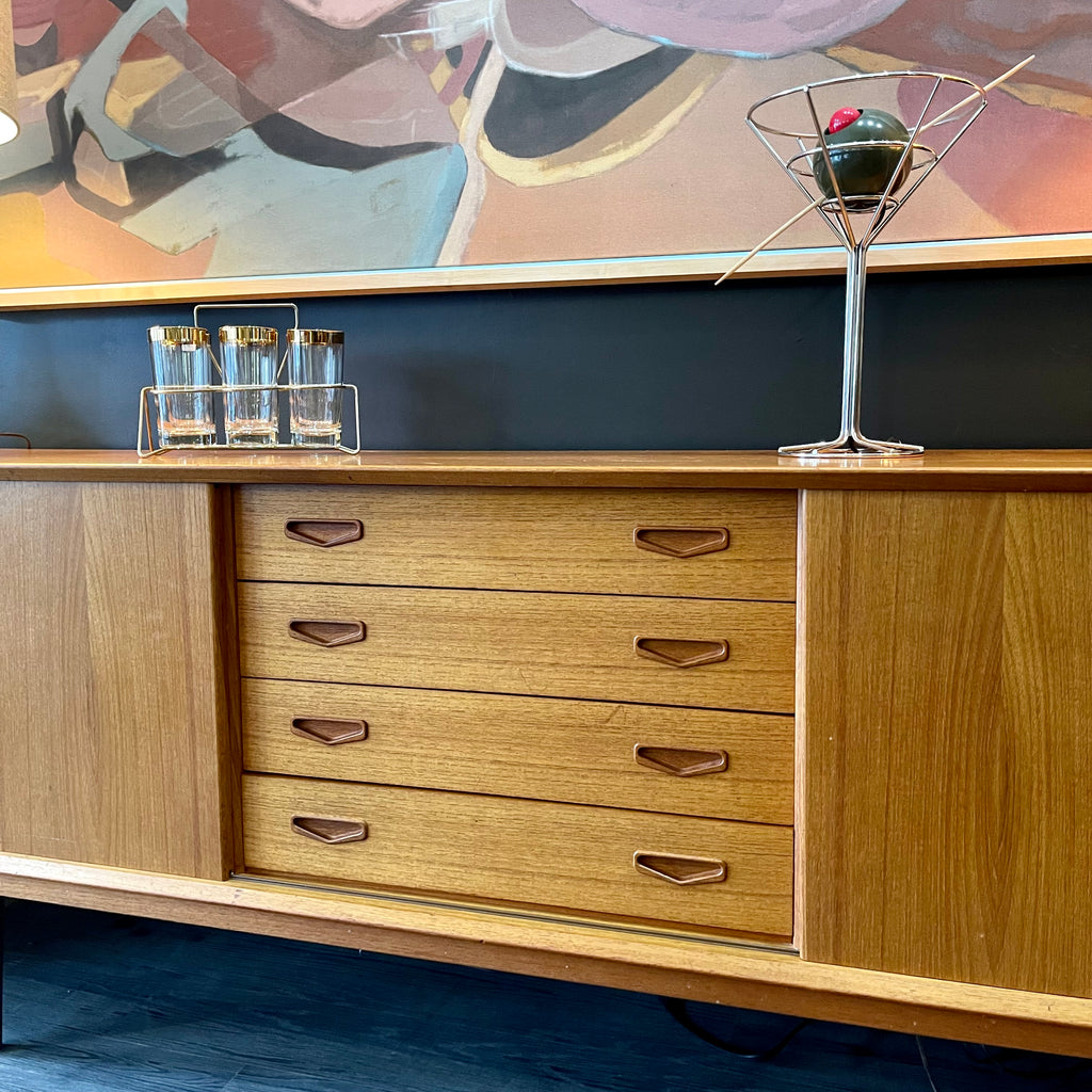 1960s Danish Teak Credenza is a beautiful blend of mid-century design and functionality. Crafted from teak, it features two sliding doors on either side that open to reveal ample storage space with adjustable shelving
