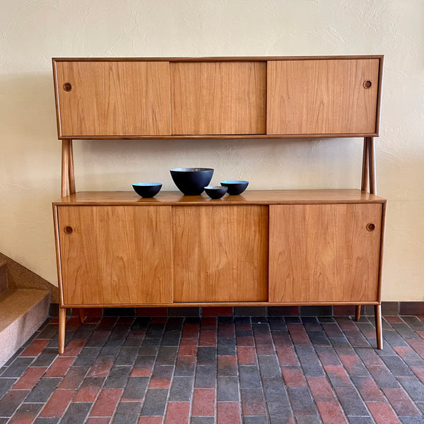 Two-tier Teak Danish Sideboard Credenza. The upper tier hosts a cabinet with sliding doors for storage. Below, sliding doors open to compartments with adjustable shelves, and drawers for small items. Solid sculptural teak legs tie the piece together. | Mr. Mansfield Vintage.