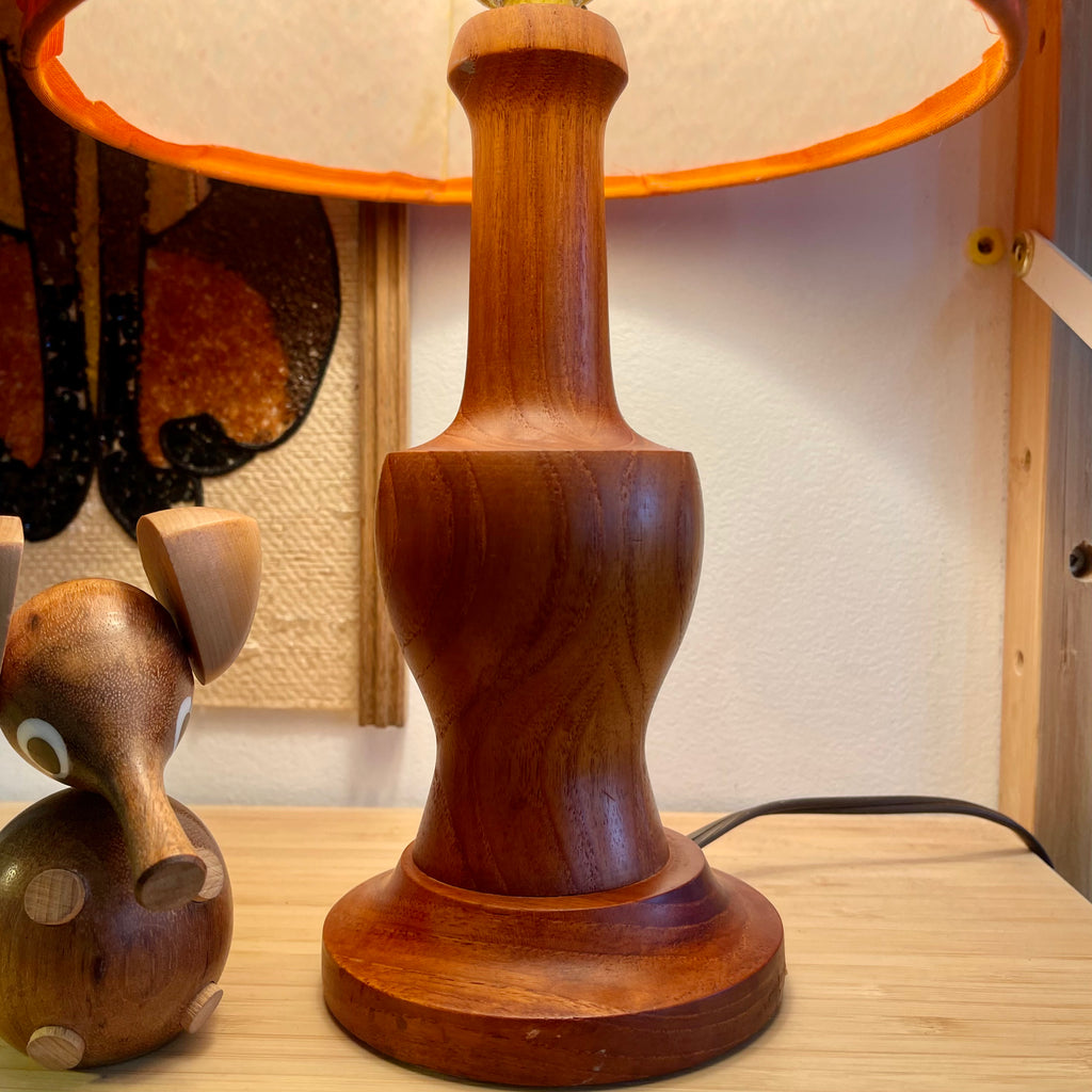 This small vintage solid teak lamp exudes mid-century charm. The original burnt orange shade adds a pop of retro flair, casting a soft, ambient glow.