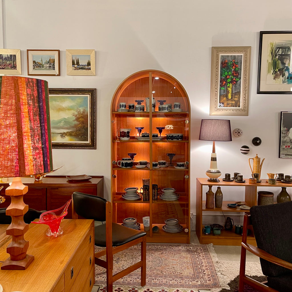 Teak display cabinet with a distinctive arched silhouette and built-in lighting, designed to showcase books, collectibles, and decorative pieces with warm ambient glow.