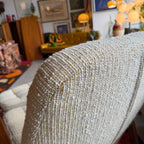 Close-up of textured beige upholstery on a vintage Huber scoop chair, featuring woven golden-yellow flecks and subtle variation in the fabric.