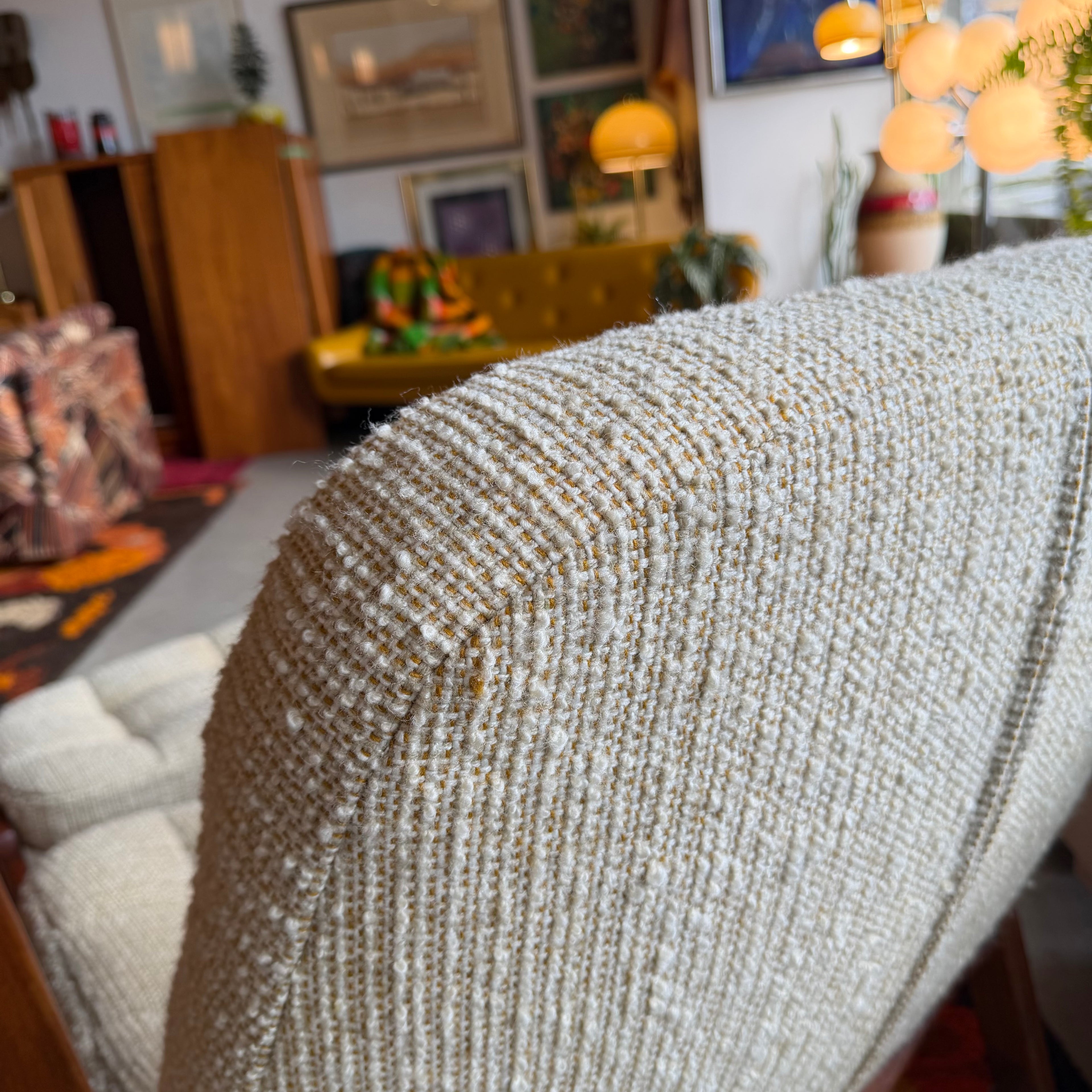 Close-up of textured beige upholstery on a vintage Huber scoop chair, featuring woven golden-yellow flecks and subtle variation in the fabric.