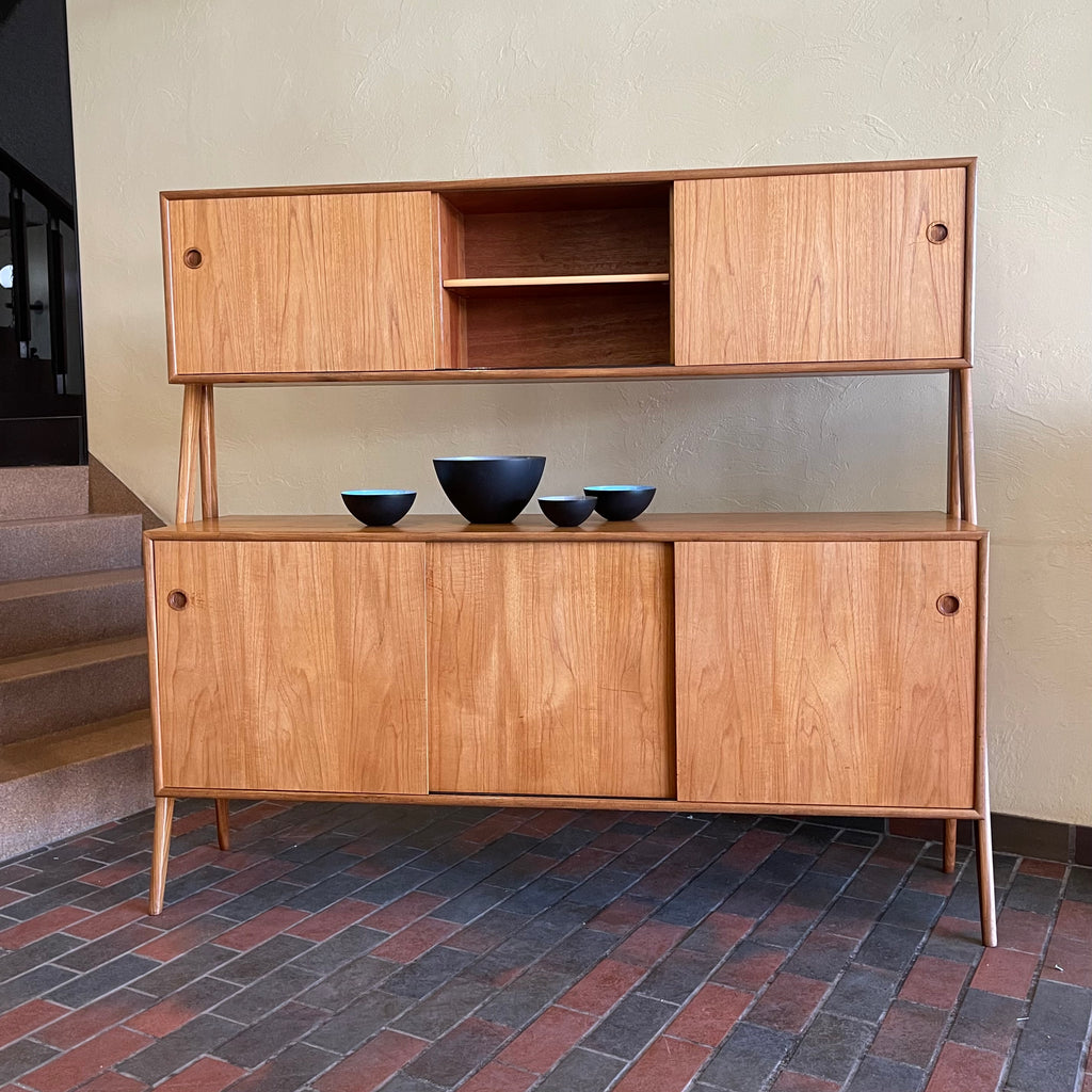 Two-tier Teak Danish Sideboard Credenza. The upper tier hosts a cabinet with sliding doors for storage. Below, sliding doors open to compartments with adjustable shelves, and drawers for small items. Solid sculptural teak legs tie the piece together. | Mr. Mansfield Vintage.