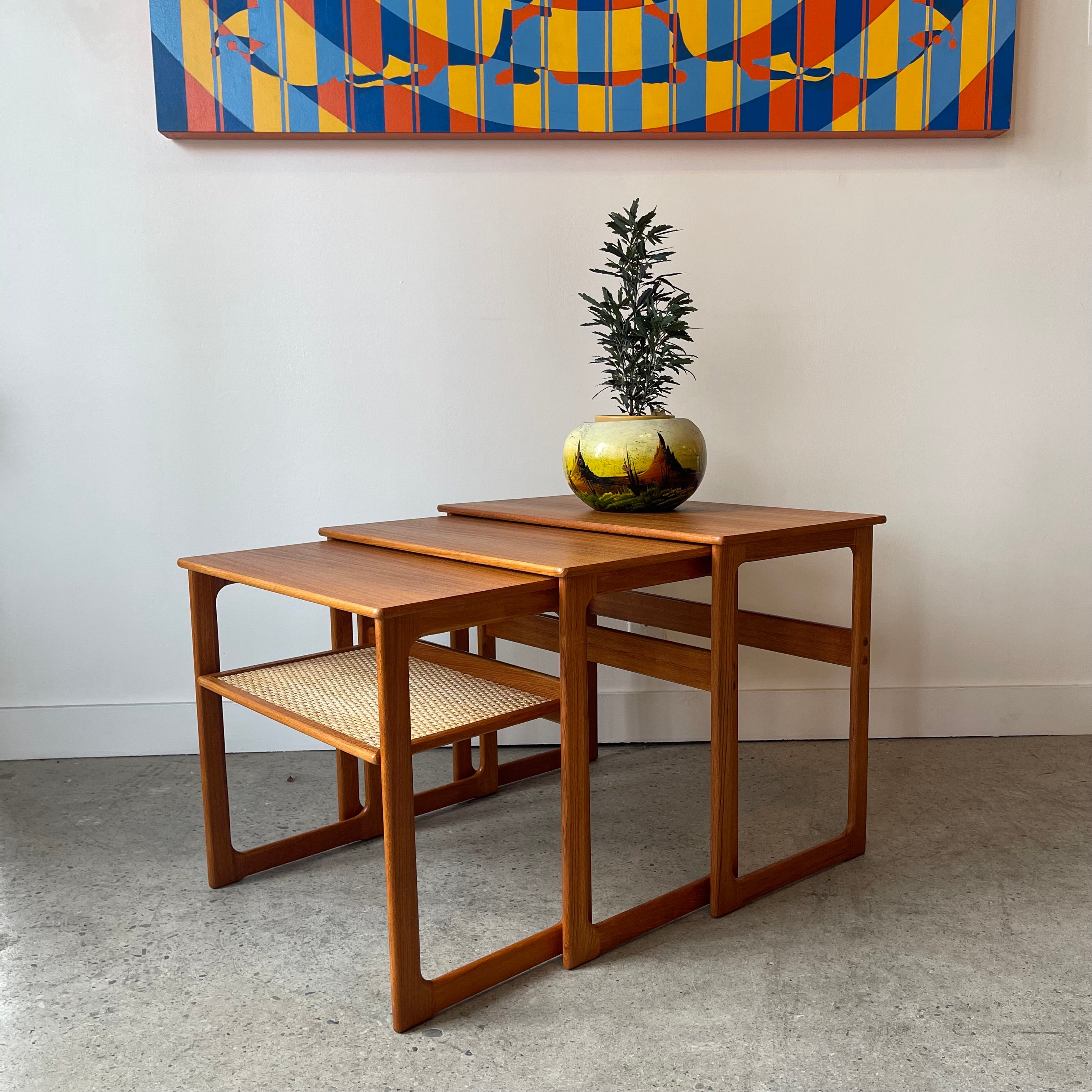 Vintage teak nesting tables with mid-century modern frames, warm wood grain and woven shelf detail