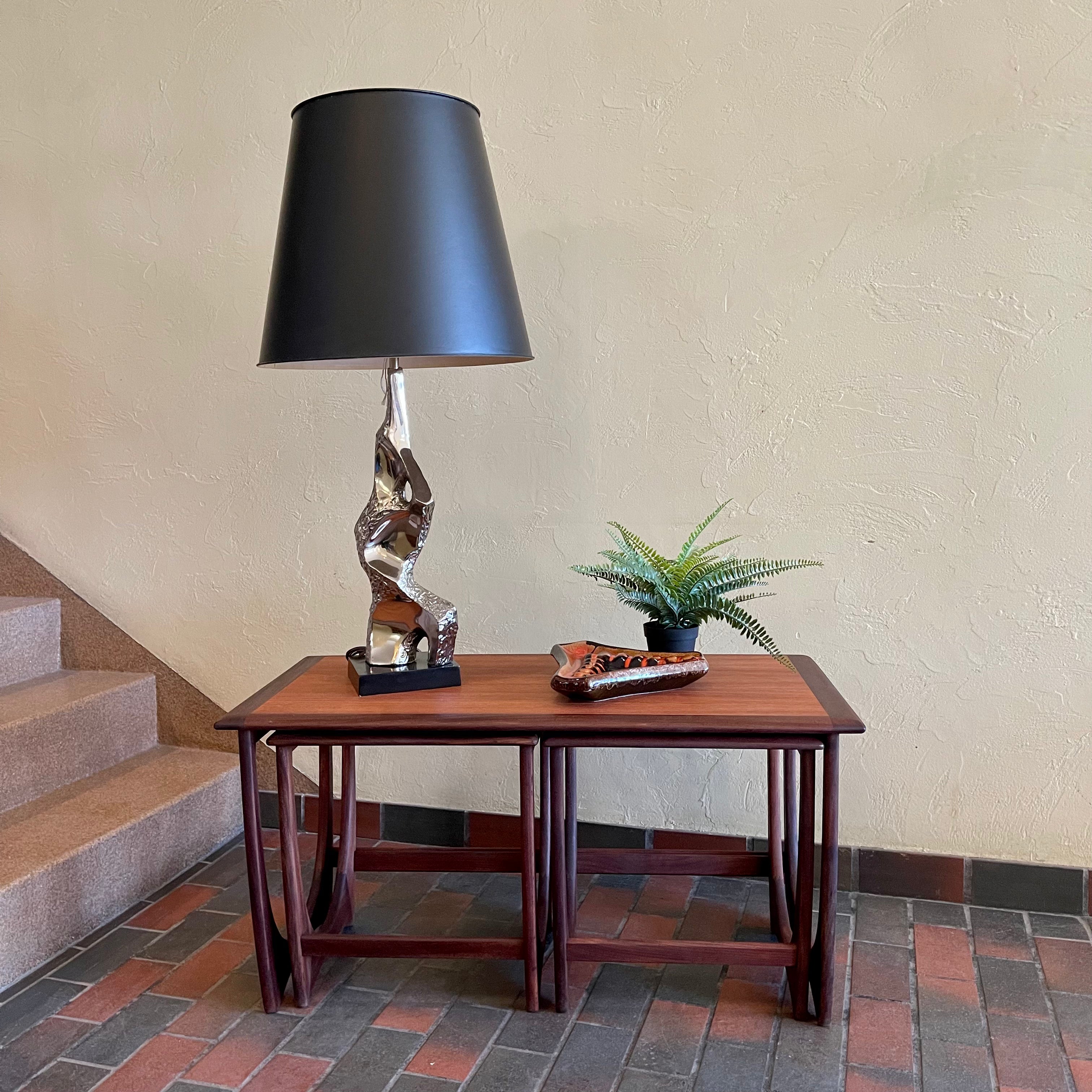 Teak G Plan nesting tables. Chrome Lamp with black shade, fern plant and an ashtray sits on top.There are 2 tables that pull out from under the main tablw. 