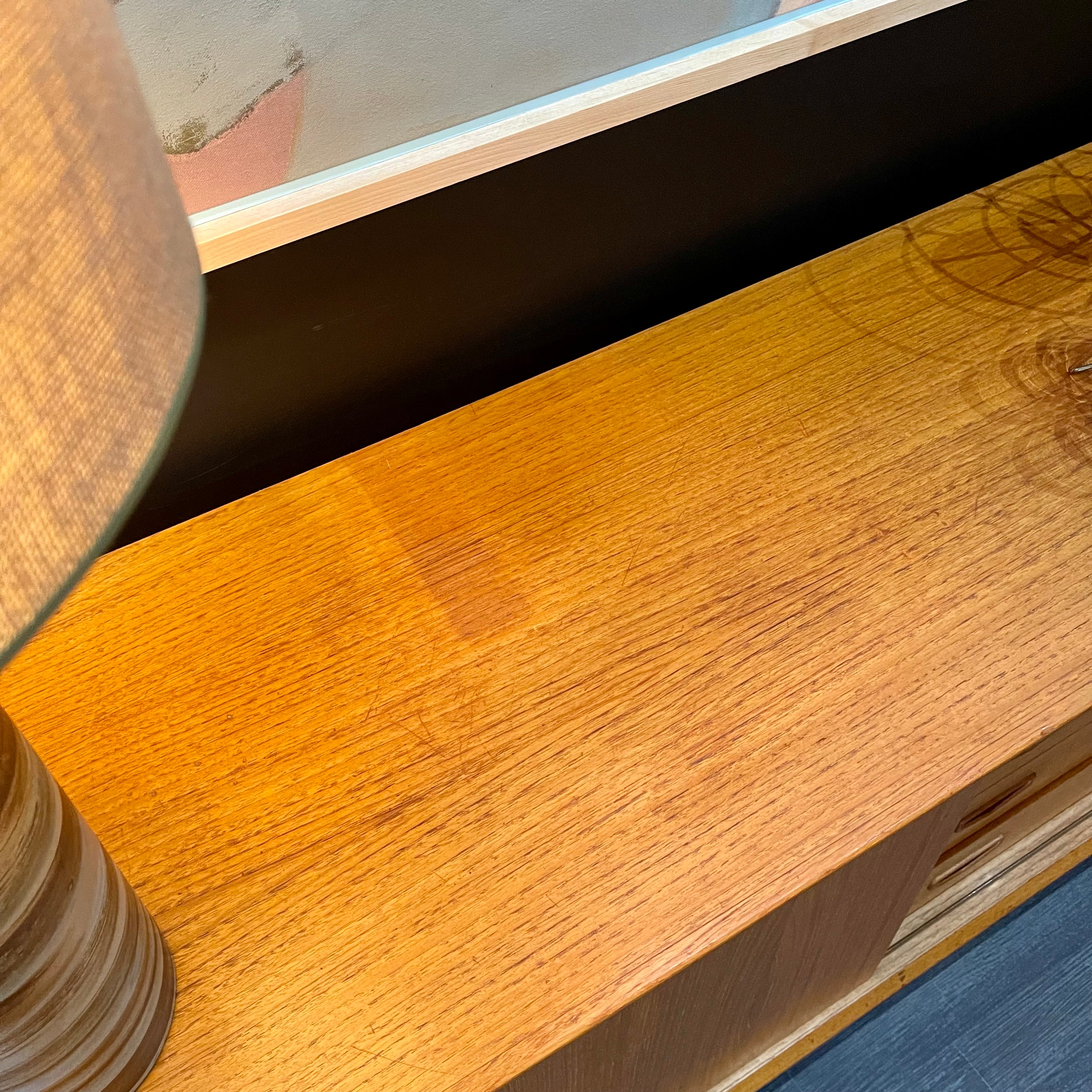 1960s Danish Teak Credenza is a beautiful blend of mid-century design and functionality. Crafted from teak, it features two sliding doors on either side that open to reveal ample storage space with adjustable shelving