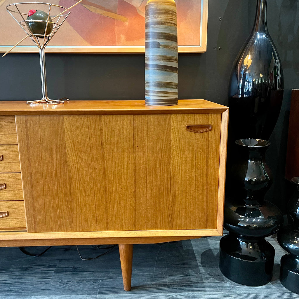 1960s Danish Teak Credenza is a beautiful blend of mid-century design and functionality. Crafted from teak, it features two sliding doors on either side that open to reveal ample storage space with adjustable shelving