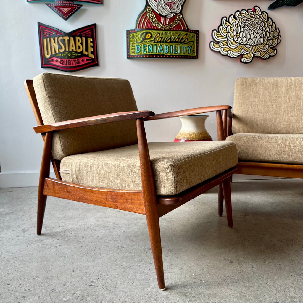 Mid-century teak lounge chairs with beige upholstered cushions, sculpted arms and tapered legs
