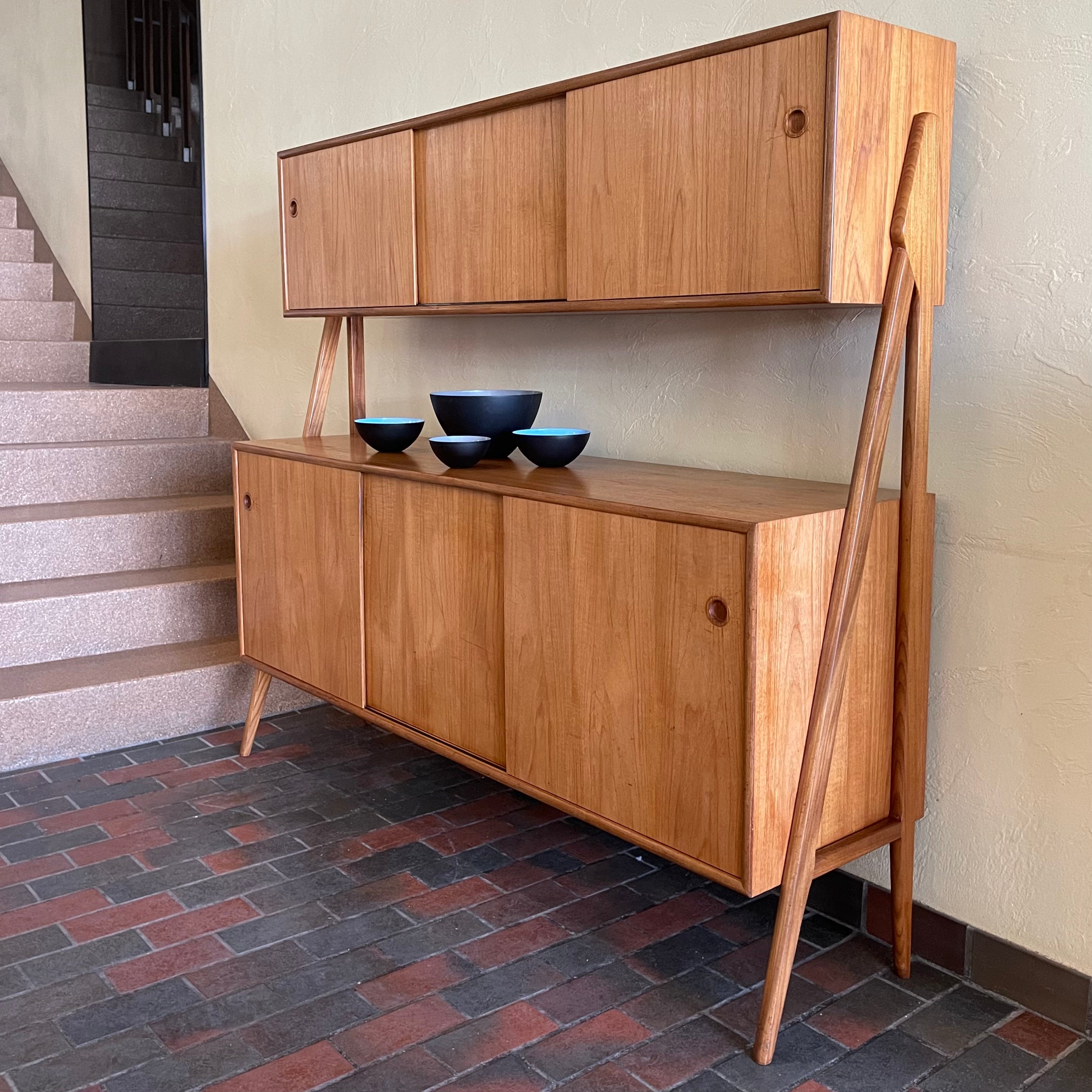Two-tier Teak Danish Sideboard Credenza. The upper tier hosts a cabinet with sliding doors for storage. Below, sliding doors open to compartments with adjustable shelves, and drawers for small items. Solid sculptural teak legs tie the piece together. | Mr. Mansfield Vintage.