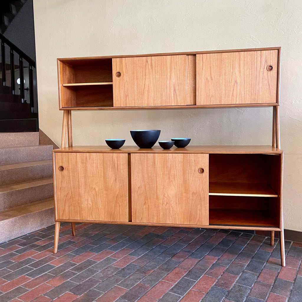 Two-tier Teak Danish Sideboard Credenza. The upper tier hosts a cabinet with sliding doors for storage. Below, sliding doors open to compartments with adjustable shelves, and drawers for small items. Solid sculptural teak legs tie the piece together. | Mr. Mansfield Vintage.
