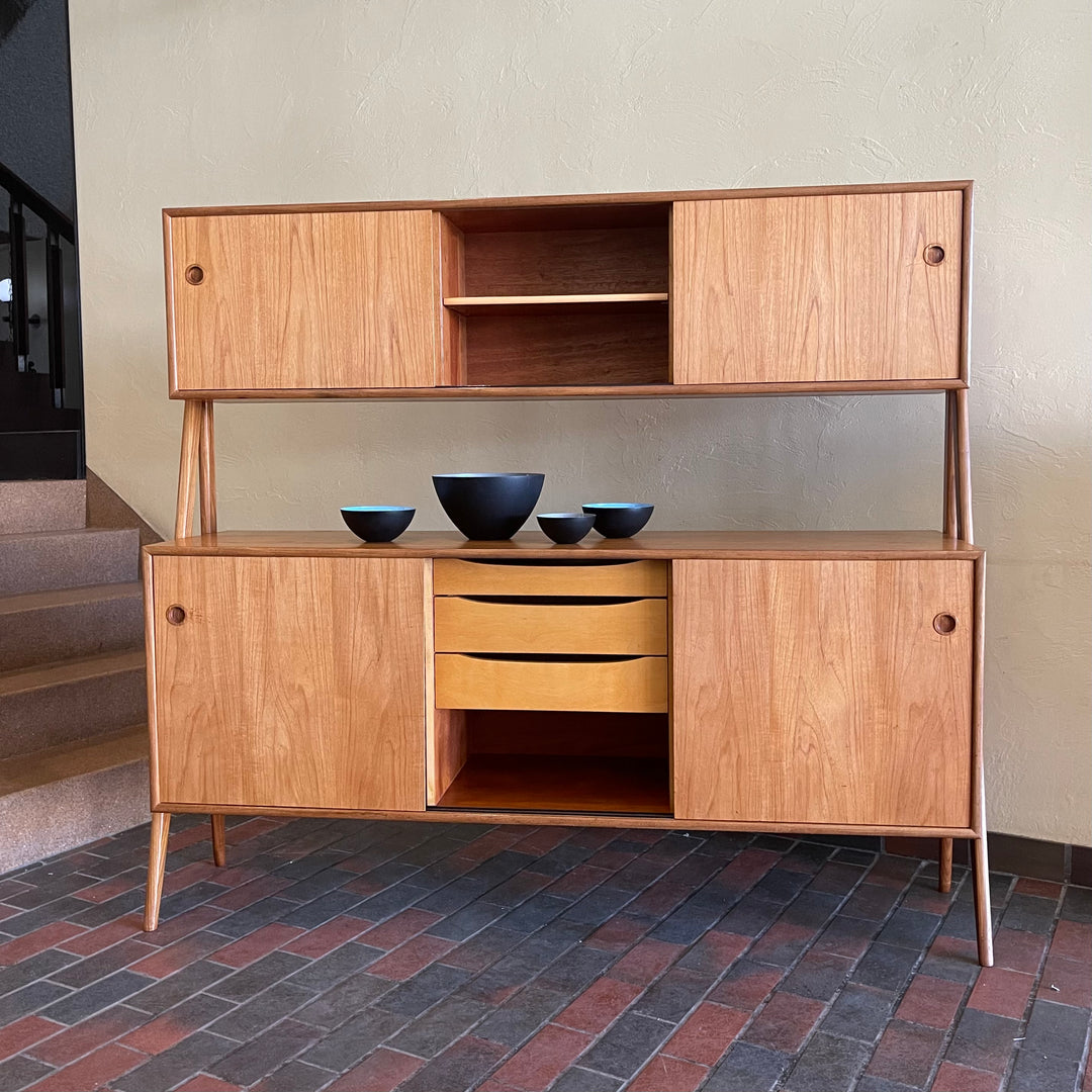 Two-tier Teak Danish Sideboard Credenza. The upper tier hosts a cabinet with sliding doors for storage. Below, sliding doors open to compartments with adjustable shelves, and drawers for small items. Solid sculptural teak legs tie the piece together. | Mr. Mansfield Vintage.