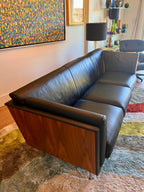 Angled view of Mark Goetz sofa showing walnut outer shell and black leather upholstery